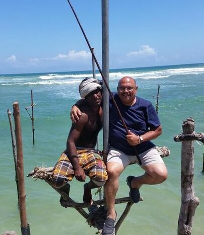 Pieter Siebel (tour guide) sitting on fishing stilt with fishing stick next to a local stilt fisherman